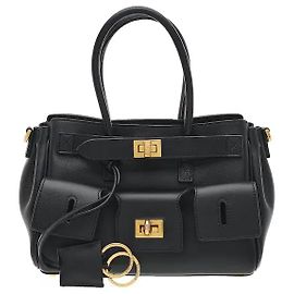 Balenciaga Confeccionado en piel suave y lisa, ofrece una textura lujosa, con detalles de cinturón en la parte delantera y el grabado del logotipo que añaden un toque sofisticado. A pesar de su tamaño mini, la amplia apertura y