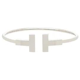 Tiffany & Co Questo bracciale combina l'iconica forma a T dell'alfabeto di Tiffany con un design a filo per un look moderno e audace. La sua struttura a filo tridimensionale e flessibile avvolge delicatamente il polso, offrendo un