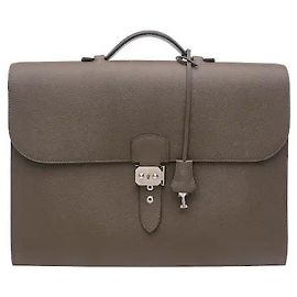 Hermès Ein Produkt, das sich durch eine klassische rechteckige Silhouette und das charakteristische Juwelen-Verschlussdetail der Marke auszeichnet. Der stabil geformte Korpus und der einzelne obere Griff verleihen eine gepflegte, luxuriöse Atmosphäre, und das